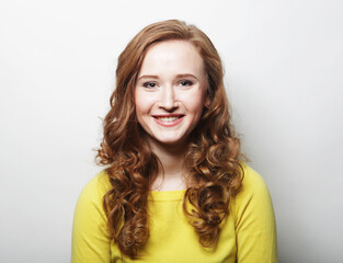 Pretty young woman with curly hair and cute smile poses alone against white background.