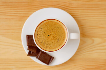 Top View of a Cup of Frothy Espresso with Dark Chocolate Chunks Isolated on Wooden Table