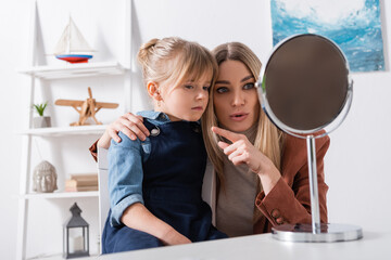 Speech therapist pointing with finger near pupil and mirror in classroom.