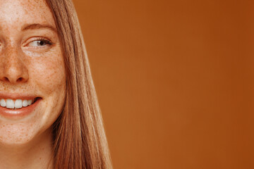 Half face beauty portrait of slim redhead beautiful happy smiling model with freckles and ginger...