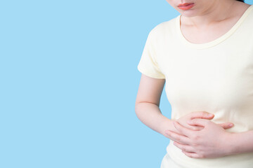 Woman suffering from stomach ache and feeling unwell over blue background. Gastrointestinal...