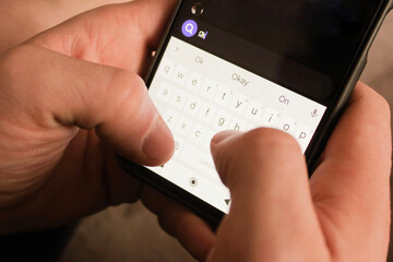 Positive casual man holding phone, smiling and giving thumbs up while wearing blue shirt, standing on white studio background
