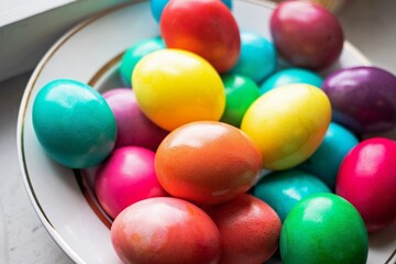 painted multi-colored chicken eggs in a wide white plate as a symbol of the holiday of Catholic believers