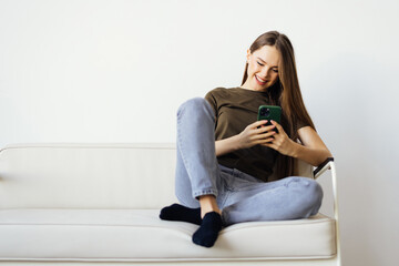 Attractive smiling woman using smart phone while sitting on the sofa at home. Communication and coziness concept.
