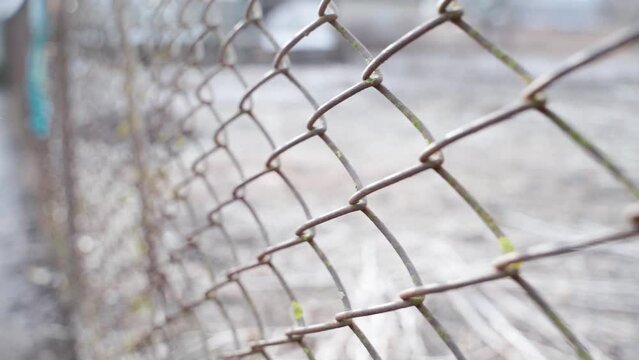 The camera moves along the old rusty mesh fence close-up. Blurred background.