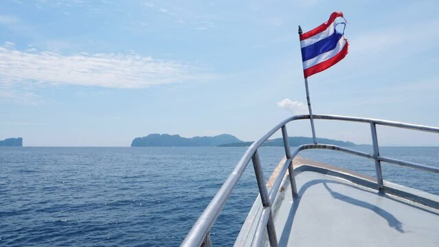 Ferry boat sail to Phi Phi archipelago, PhiPhi Don island in sight straight ahead. Thai flag tremble on wind at fore of vessel, calm blue sea waters around, slow motion shot