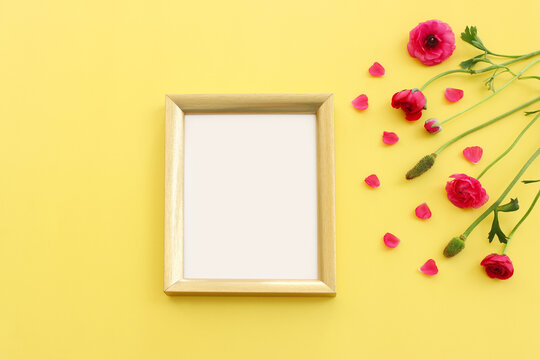 Top view image of pink flowers composition and empty gold photo frame over yellow pastel background