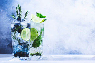 Summer cocktails or mocktails and cold drinks. Refreshing mojito drink with blueberries, blackberries, raspberries and  lime, herbs and ice on gray background - obrazy, fototapety, plakaty