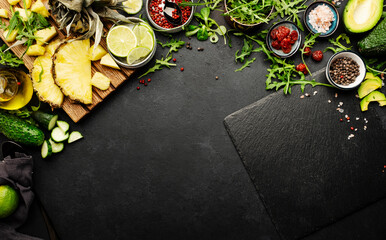 Healthy clean eating food layout and diet nutrition concept. Pineapple, vegetables, dried fruits, greens and other ingredients for salad preparation on black table background with slate board