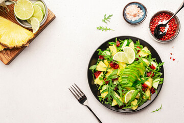 Vegan vegetarian salad with pineapple, arugula, avocado and dried cherry on white stone kitchen table, top view. Healthy eating, clean diet food, weight loss concept