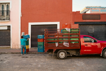 red pickup truck parked near the door. Man working unloading boxes turned back unrecognizable. Everyday life on streets of a mexican city valladolid