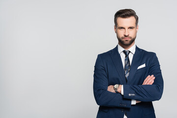 bearded businessman in blue blazer standing with crossed arms isolated on grey.