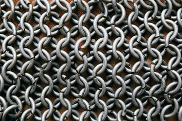 Flat lay view of chain mail armor on brown leather. Metallic background.
