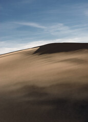 Deserted landscape. Sand dune with dark shadow on a background of blue sky.