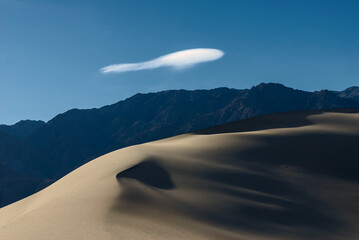Deserted landscape. Sand dune with dark shadow on a background of blue sky.