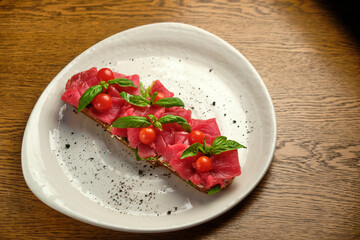 Bruschetta with red pickled meat on a white plate