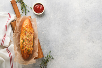 Baguette boats. Hot baked sandwich on baguette bread with ham, bacon, vegetables and cheese on parchment and wooden stand on gray concrete background. Top view. Copy space.