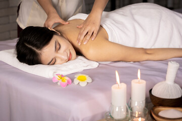 Fototapeta na wymiar Healthy Asian Thailand woman lying in bed doing spa treatment on her back. was compressed with herbs wrapped in a white cloth massage her back to relax There were flowers and candles on the bed.