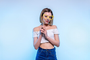 Young caucasian girl with light blue eyes looks in camera with funny glasses - Studio photography of pretty woman having fun with fake eyewear