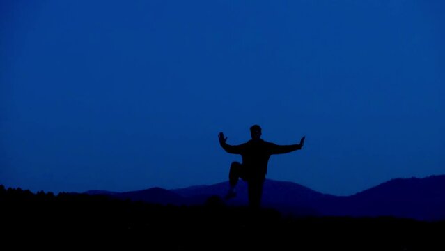 Wushu master trains maritial arts in the evening against dark sky