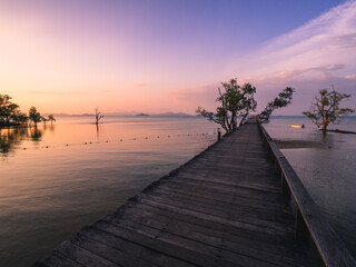 Scenic view of sea with infinity long wooden bridge pier boardwalk over peaceful bay of water in sunset orange sky. Koh Mak Island, Trat Province, Thailand.