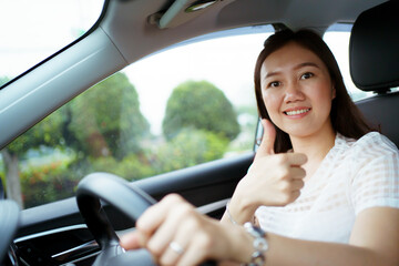 Happy Asian woman driving the electric vehicle - EV car smiling and showing her thumb up.