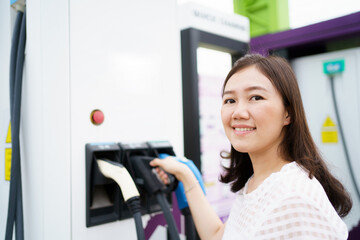 Fototapeta na wymiar Happy Asian woman holding a DC - CCS type 2 EV charging connector at EV charging station.