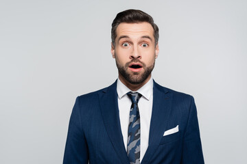 amazed businessman in blue blazer looking at camera isolated on grey.