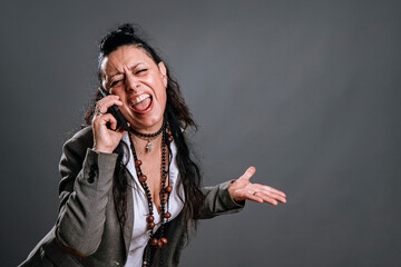 middle-aged woman with defiant attitude screams while attending to her mobile in study shot on gray...