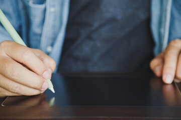 Close up a man in casual clothes using a electronic pen on a blank tablet on the wooden table