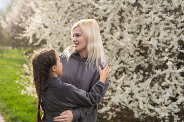 Woman walking with daughter in blooming spring garden exploring flowering tree. Family admires nature.