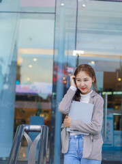 A female Asian student standing in front of a mall holding a tablet during school breaks and the idea of studying online via the Internet outside the home.