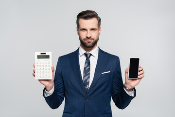 economist in blue suit showing calculator and smartphone with blank screen isolated on grey.