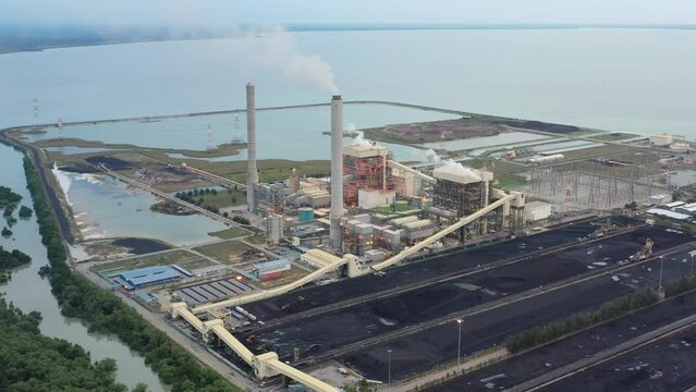 High angle pull out shot capturing large coalfield and industrial ultra-supercritical coal-fired power plant with smokes raising from chimney located at costal area of Manjung, Perak, Malaysia.