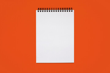 Notebook made of white paper with binding on a orange background. Blank notepad with free space for text. Notebook in classic binding without notes, top view