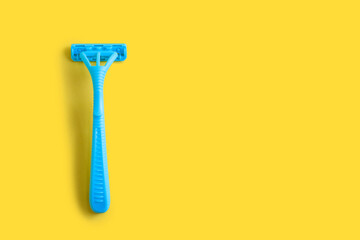 Disposable plastic razor on a yellow isolated background. Blue women's razor with free space for text on a white background. Skin care razor and neat look concept