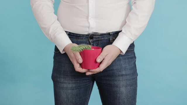 A man on a blue background holds a red pot with a cactus in his hands. Cognitive low libido in men, impotence. Sexual diseases