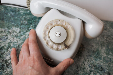 A hand touches an old analog white Soviet telephone on a blue textured table top and a white...