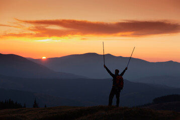 Tourist in mountains at sunset. Orange sky. Silhouette of mountains peaks