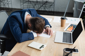 tired economist sleeping at workplace near calculator and laptop with blank screen.