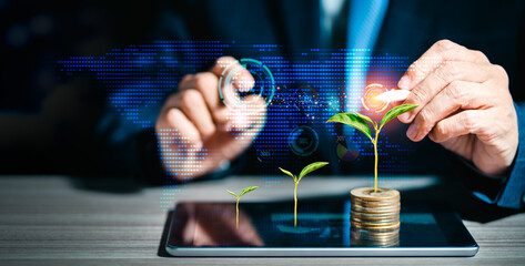 Businessman is touching virtual screen icons and stacking coins with growing tree on the tablet computer