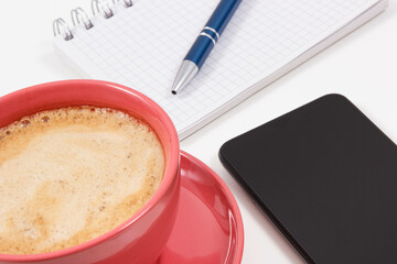 Mobile phone, coffee with milk and notepad for writing notes. White background