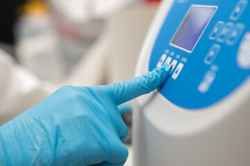 Close up laboratory worker hand in rubber gloves sets parameters on the centrifuge for sample preparation. DNA, oncology marker analysis in the clinical laboratory.