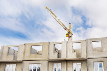 A large tower crane builds a house against a blue sky with clouds. Construction of an apartment building