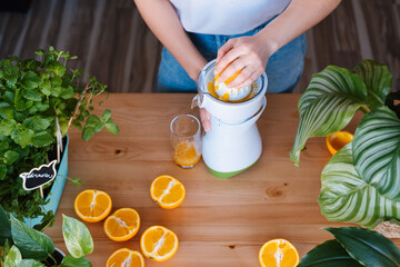 Woman making fresh orange juice in a kitchen full of plants.
