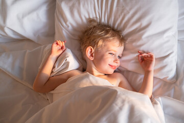 Pretty toddler boy just woke up and basking in bed.