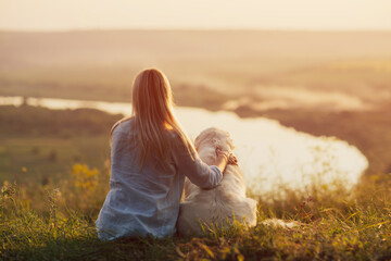 A young woman with a golden retriever dog watching the sunset on the hill.