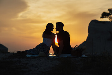 Dark silhouette of couple in love at picnic against the backdrop of a orange sunset in the mountains. Romantic time. 