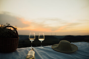White wine bottle, wine glasses, basket with white flowers and straw hat at the summer picnic at...