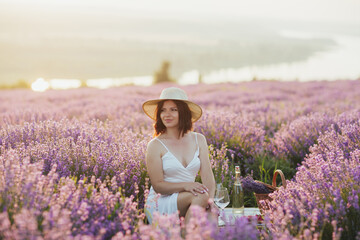 Fototapeta na wymiar Woman with straw hat sitting on the picnic in lavender field. The summer season. 